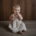 Bébé assis mordant un anneau de dentition bretzel Mushie beige