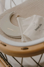 Un marqueur de jalon en bois en bois de croissant de lune carte étape bébé avec 1 mois (1 mois) à côté d'un sac en tissu blanc étiqueté Amour fou repose sur une couverture de bébé beige texturée à l'intérieur d'un berceau zakuw.