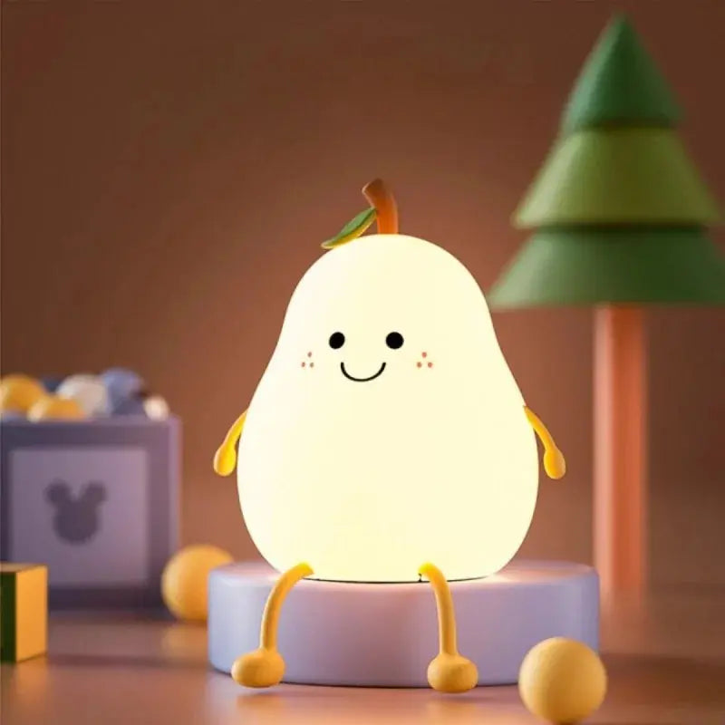 Une veilleuse mignonne et brillante en forme de poire de la marque Marys avec un visage souriant, de minuscules bras et des jambes est assise sur une plate-forme ronde. En arrière-plan se trouve un arbre  et une boîte avec un visage d'ours, ainsi que des boules jaunes éparpillées.
