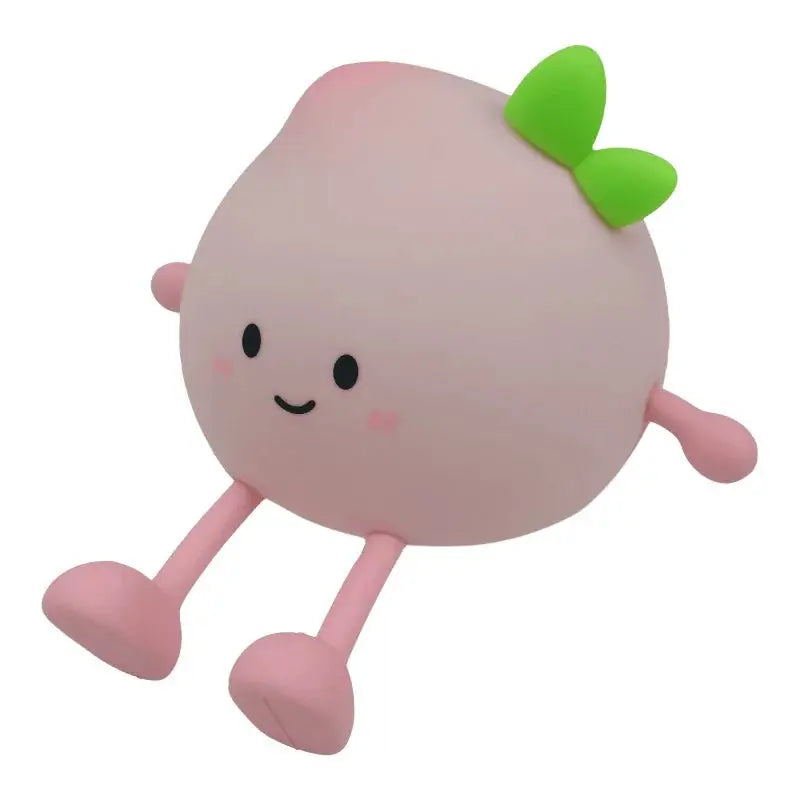 Un personnage rond et rose de la marque Mary's avec un visage souriant, des joues roses, une feuille verte sur le dessus et de longs bras et jambes, assis avec les jambes tendues - comme une pêche - veilleuse rechargeable 